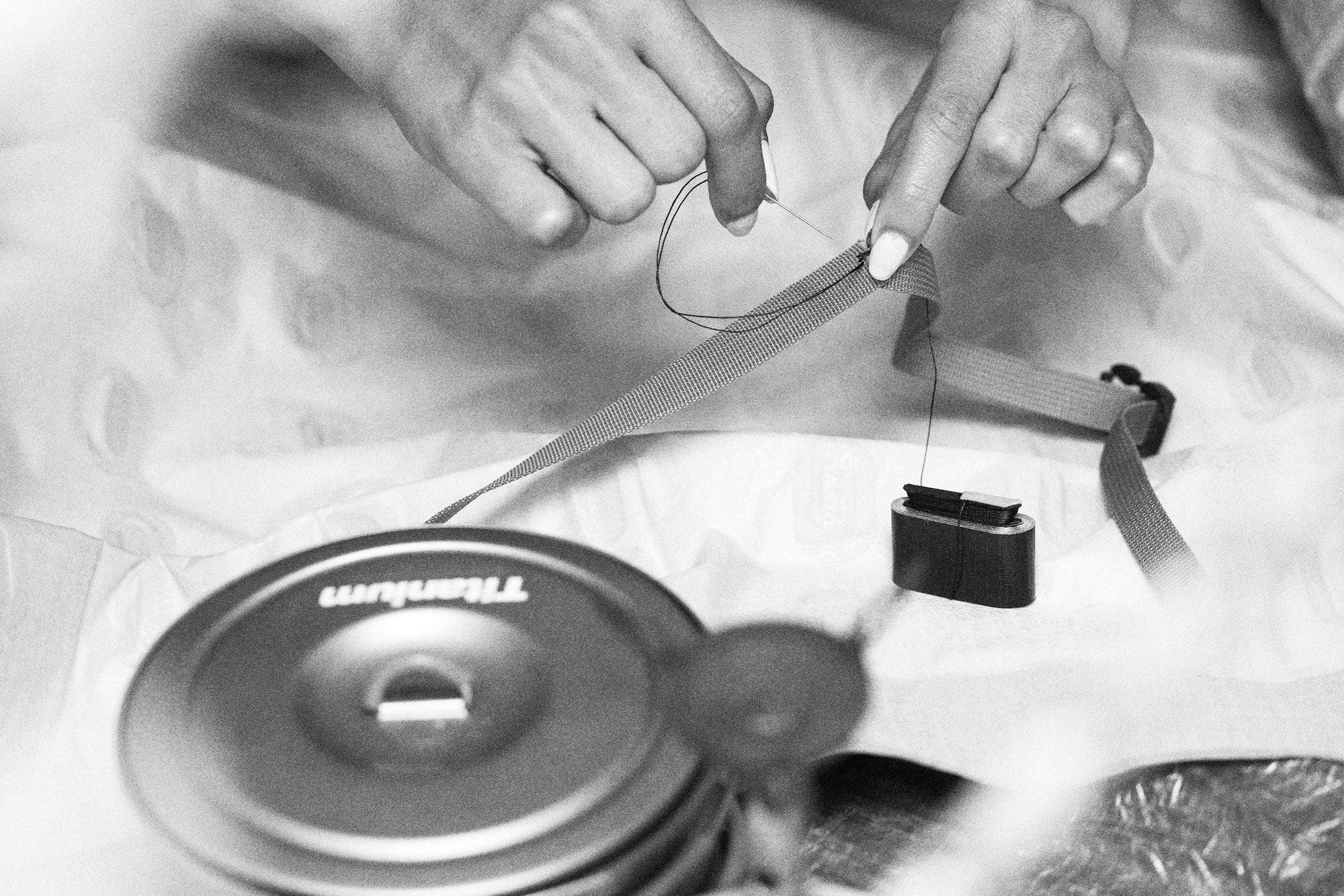 Black and white photo of hands sewing a gear repair with needle and thread