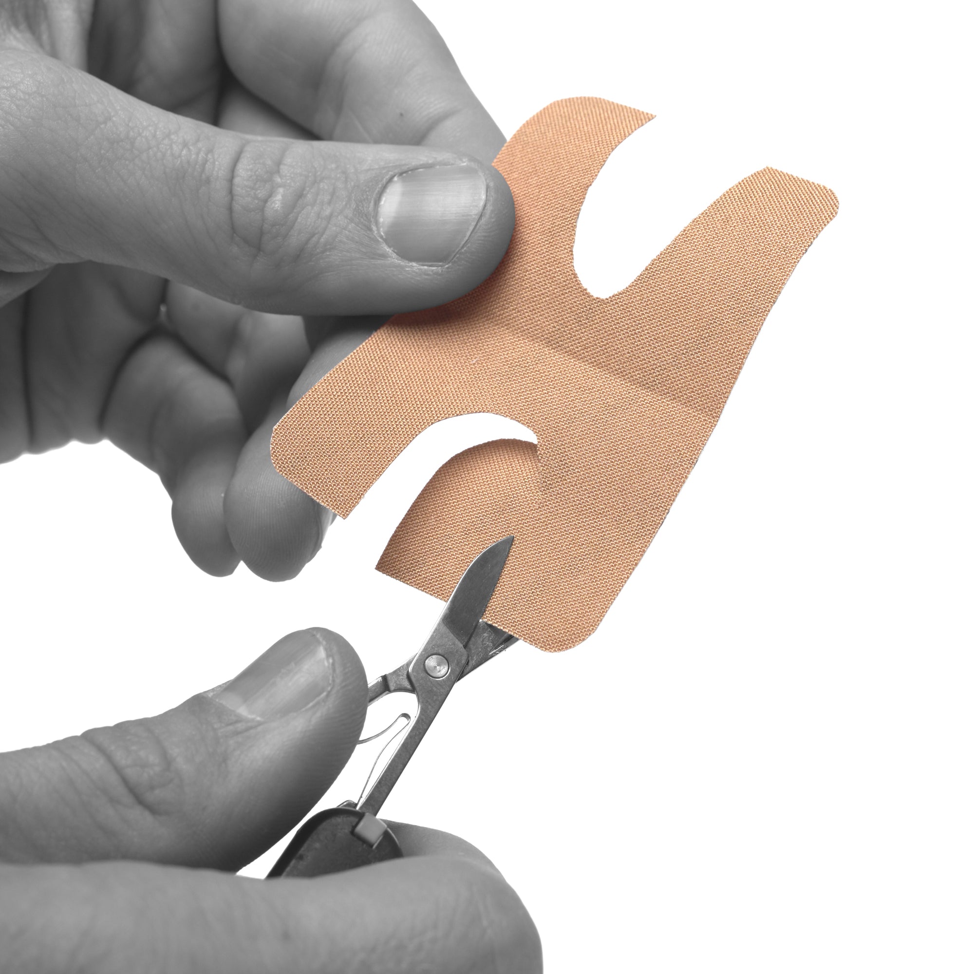 A close-up of a person's hands holding a beige adhesive bandage and cutting it with small scissors against a white background.